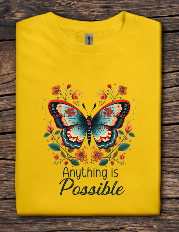 Yellow t-shirt with a butterfly design and 'Anything is Possible' text on a wooden surface