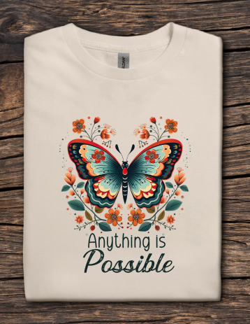 Beige t-shirt with a colorful butterfly design and 'Anything is Possible' text on a wooden surface
