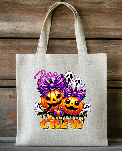 Halloween tote bag featuring smiling pumpkins with purple bows, friendly ghosts, and Boo Crew text on a natural fabric bag.