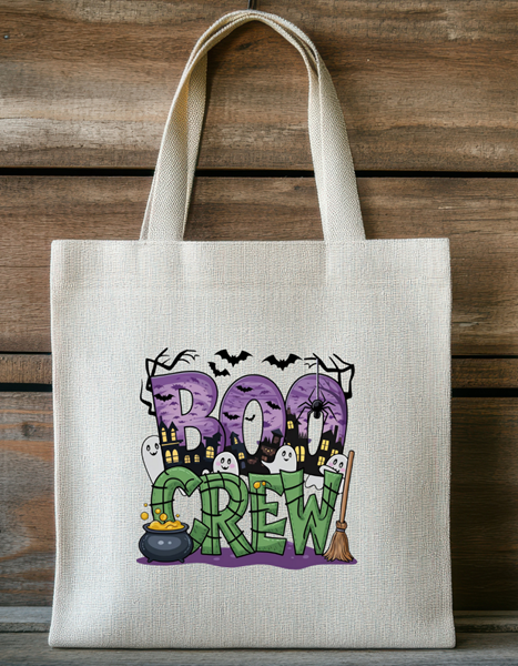 Halloween tote bag featuring Boo Crew text with cute ghosts, cauldron, broomstick, bats, and a spooky cartoon town on a natural fabric tote.