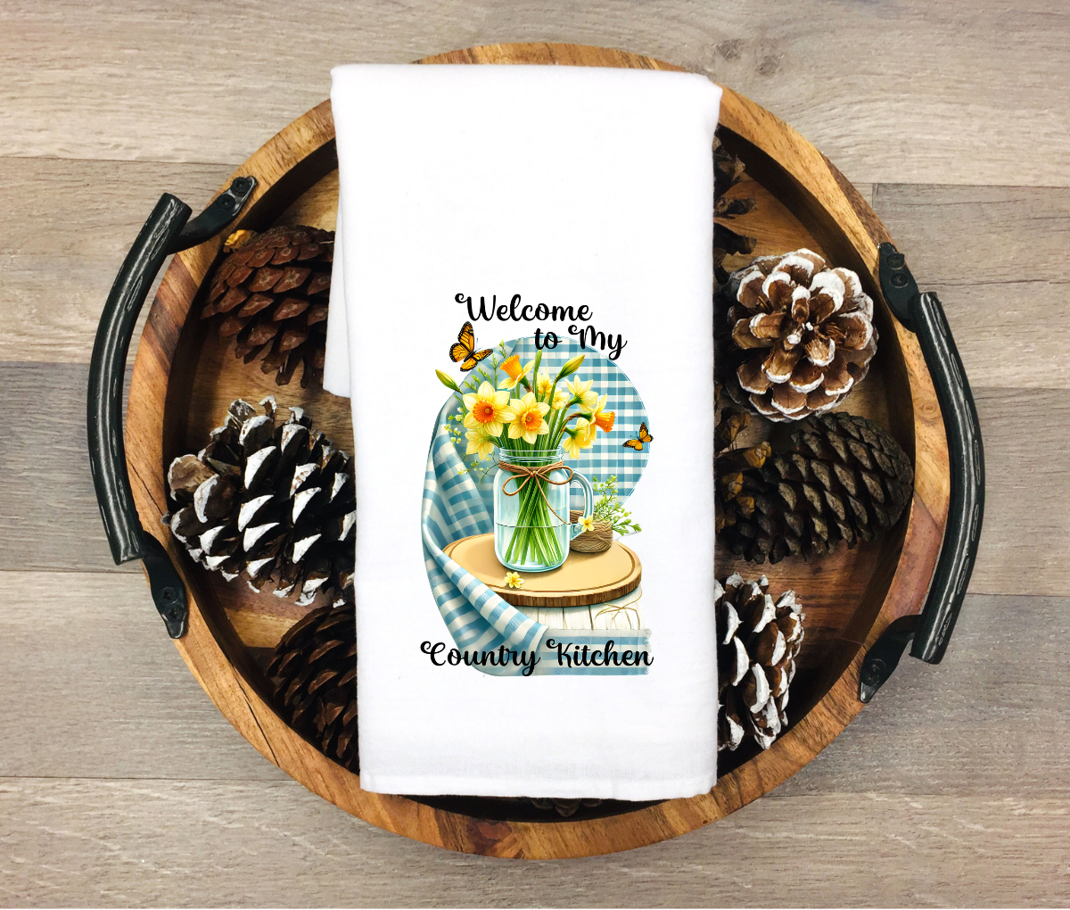 White kitchen towel featuring a mason jar with yellow daffodils, butterflies, blue gingham background and the phrase “Welcome to My Country Kitchen”
