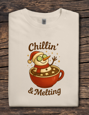 Beige t-shirt featuring a snowman relaxing in a mug of hot cocoa with the text “Chillin’ & Melting”.