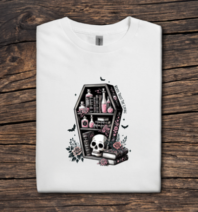 White t-shirt with a black coffin design featuring a skull and bottles on a wooden surface