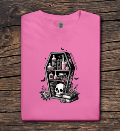 Pink t-shirt with a black coffin design featuring a skull and roses on a wooden surface