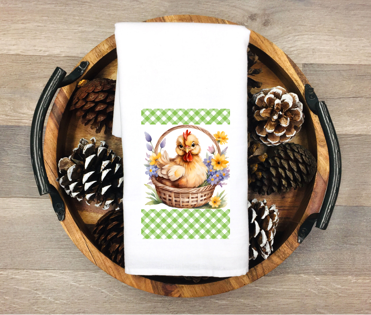 White kitchen towel featuring a hen sitting in a woven basket surrounded by flowers with green farmhouse pattern accents