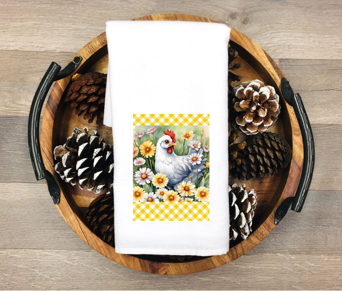 White kitchen towel featuring a white hen surrounded by daisies and wildflowers with yellow farmhouse pattern accents