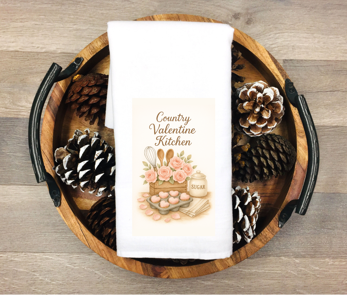 White kitchen towel featuring heart-shaped cookies, roses, baking utensils and a sugar jar with the phrase “Country Valentine Kitchen”