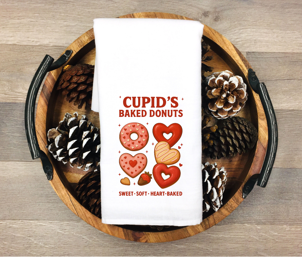 White kitchen towel featuring heart-shaped donuts and Valentine treats with the phrase “Cupid’s Baked Donuts Sweet Soft Heart-Baked”