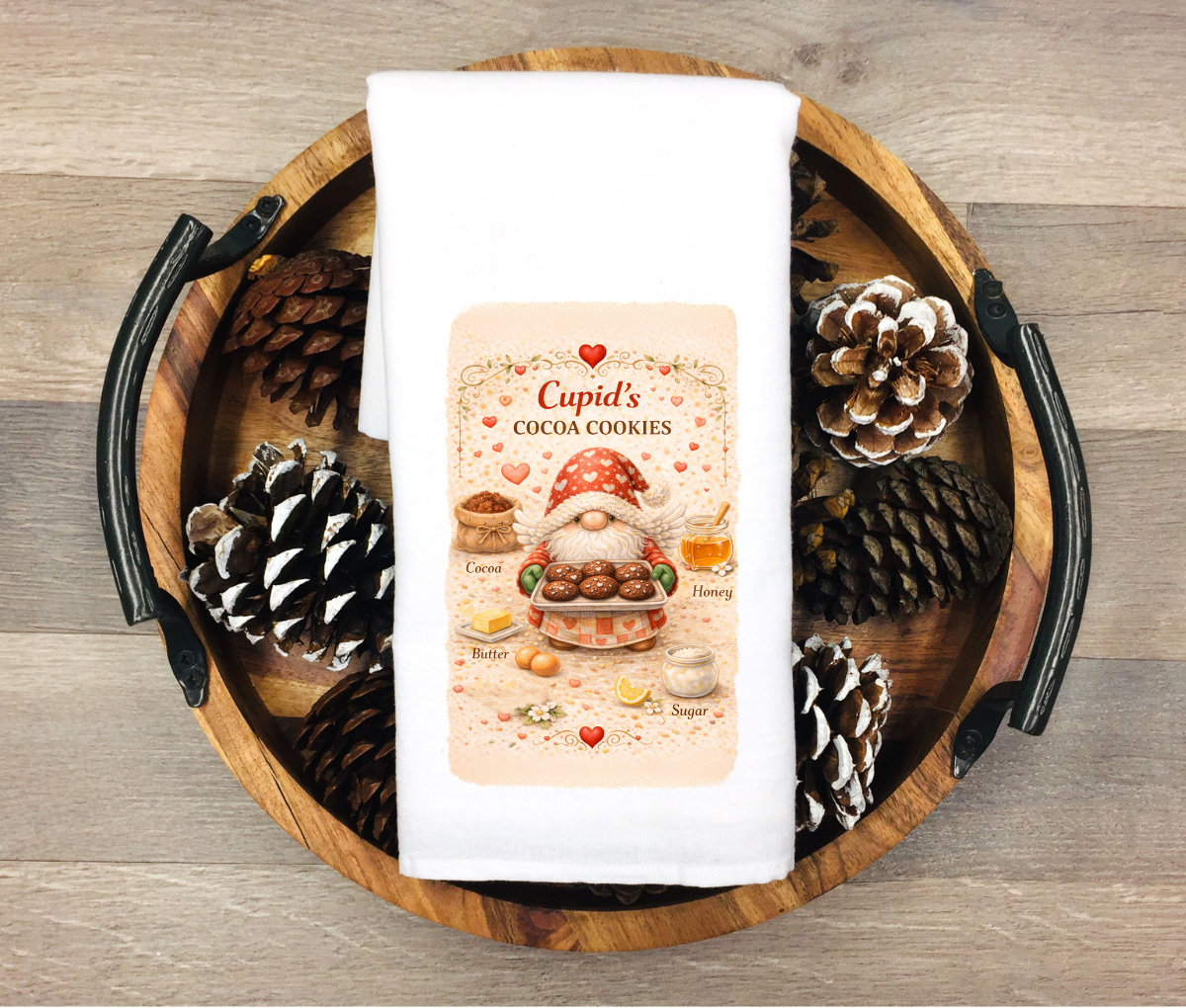 Cupid-themed kitchen towel on a wooden tray with pinecones