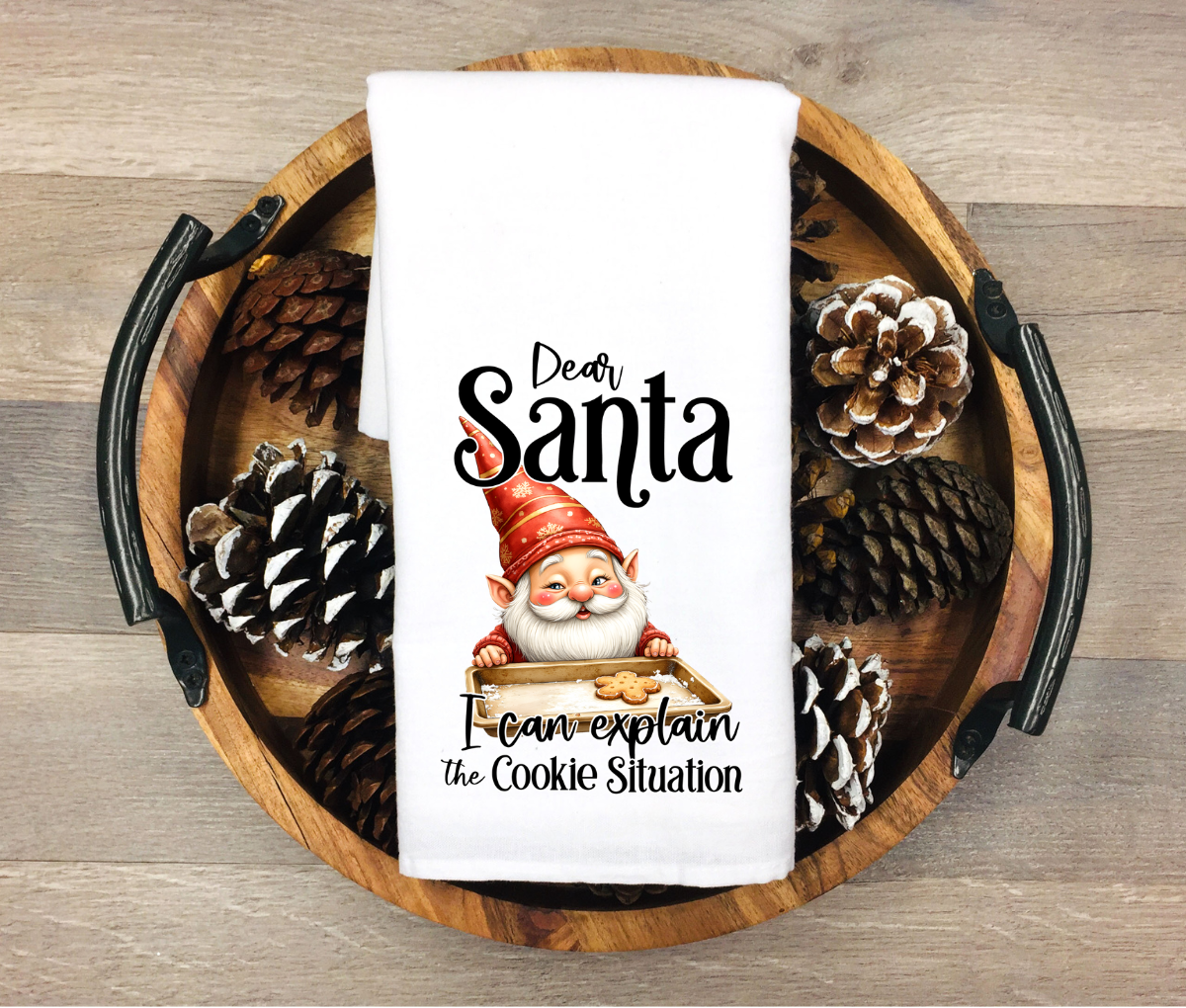 Towel with a gnome and text on a wooden tray with pinecones