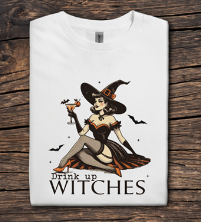 White t-shirt with a witch graphic and 'Drink up Witches' text on a wooden surface