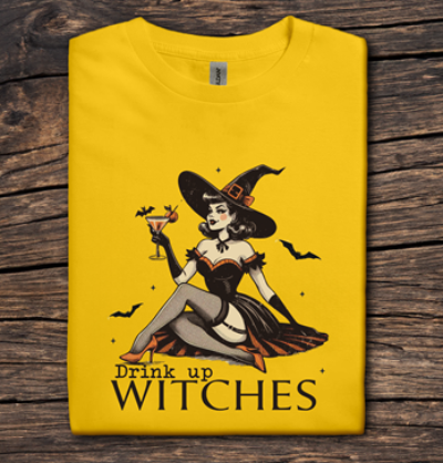 Yellow t-shirt with a witch graphic and 'Drink up Witches' text on a wooden surface