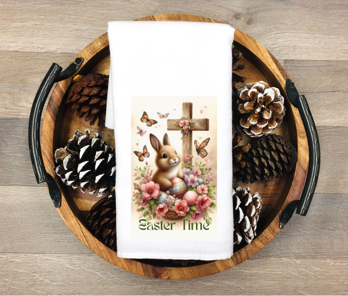 Easter-themed towel with bunny and cross design on a wooden tray with pinecones.