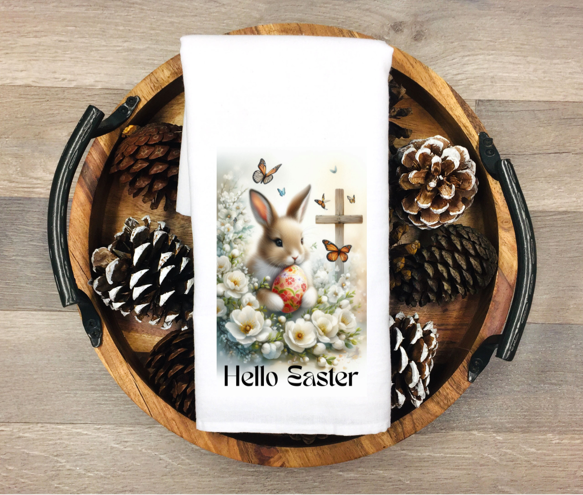 Easter-themed towel with bunny and eggs design on a wooden tray with pinecones.