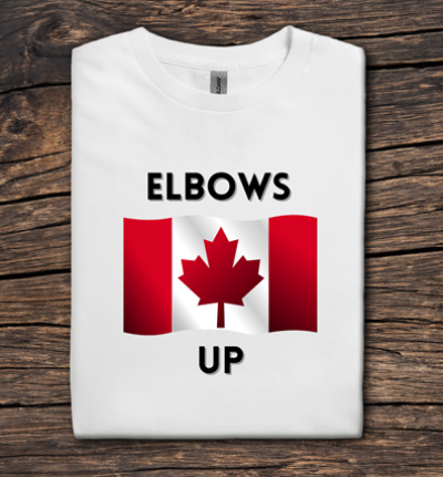 White t-shirt with Canadian flag design and text 'ELBOWS UP' on a wooden surface