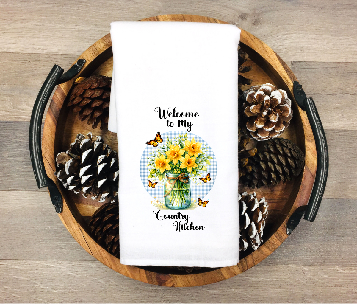 White towel with floral design and text on a wooden tray with pinecones