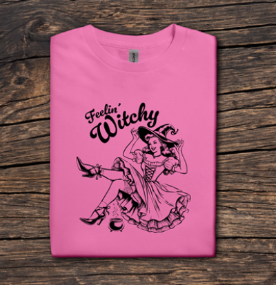 Pink t-shirt with witch graphic and 'Feelin' Witchy' text on a wooden surface