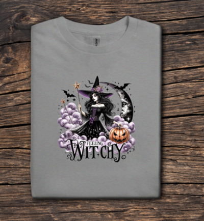 Gray t-shirt with a Halloween-themed design featuring a witch and pumpkins on a wooden surface.