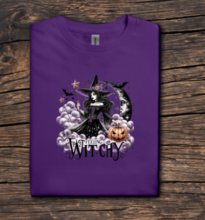 Purple t-shirt with Halloween-themed design featuring a witch and moon on a wooden surface