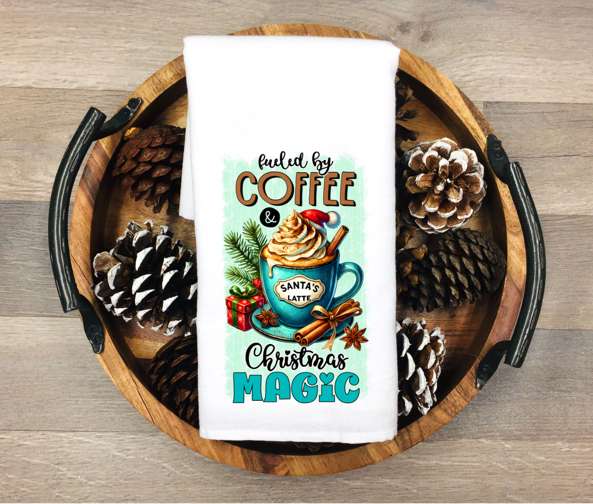 Decorative towel with Christmas design featuring a mug and pinecones on a wooden tray.