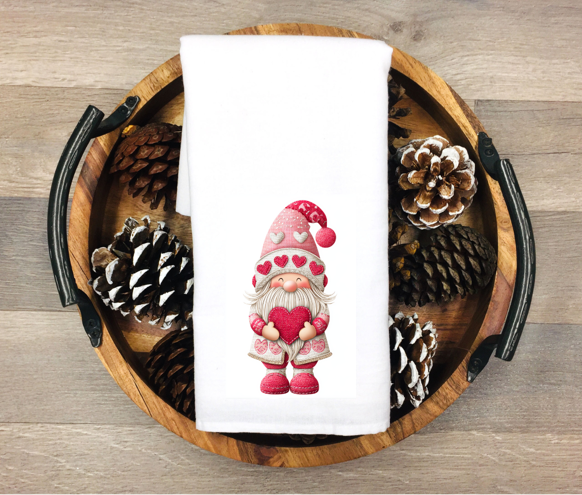 Valentine-themed towel with a gnome holding a heart, surrounded by pinecones on a wooden tray.