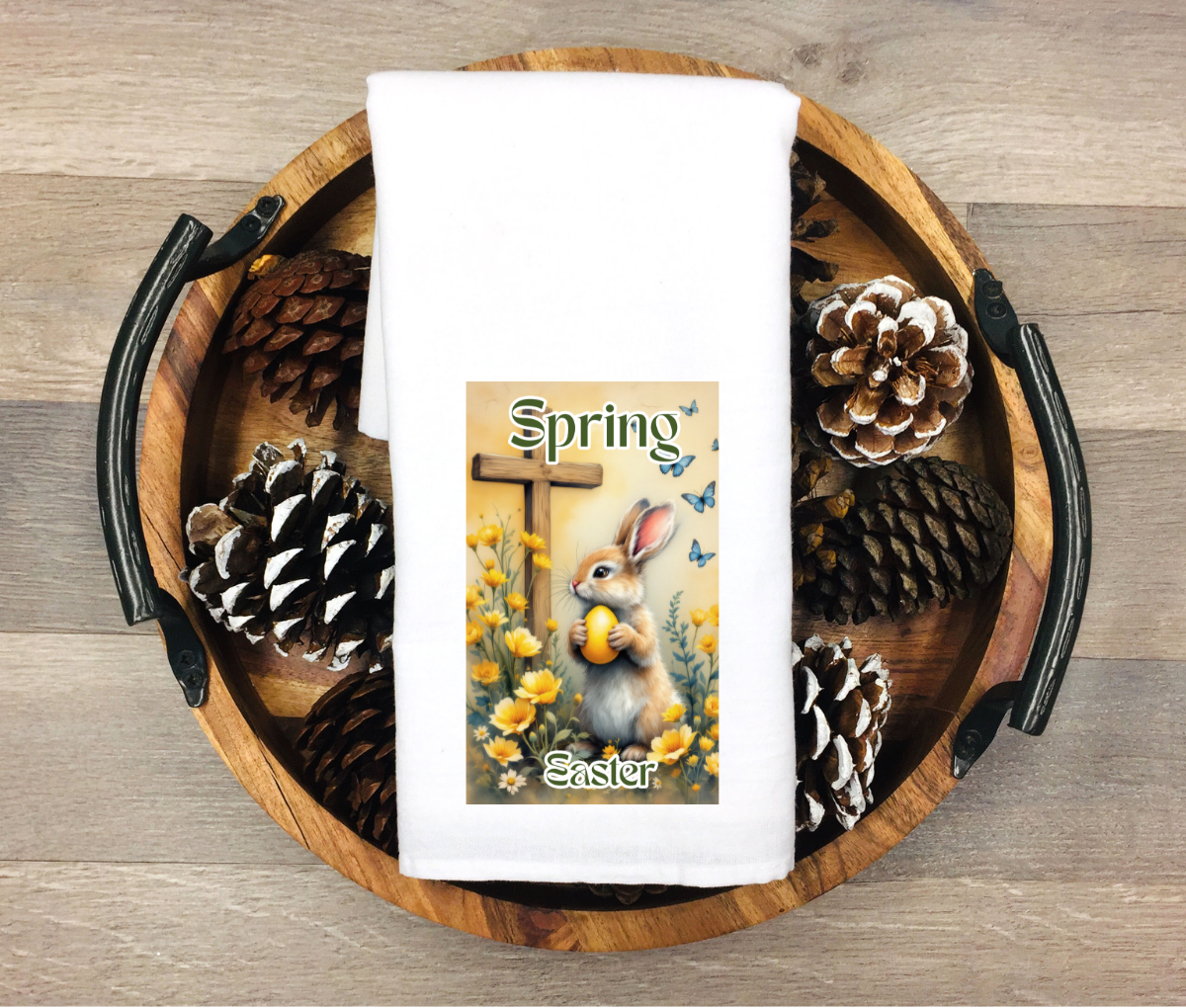 Wooden tray with decorative towel featuring a bunny and 'Spring' text, surrounded by pinecones.