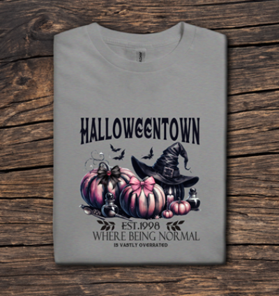 Gray t-shirt with Halloween-themed design featuring pumpkins and a witch hat on a wooden surface.