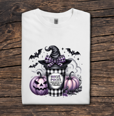 White t-shirt with Halloween-themed design featuring a witch hat, pumpkins, and a potion bottle on a wooden surface.
