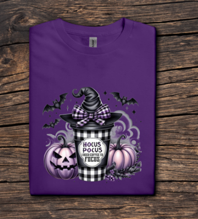 Purple t-shirt with Halloween-themed design featuring a witch hat, pumpkins, and text on a wooden surface.