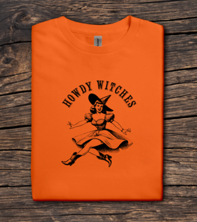 Orange t-shirt with 'Howdy Witches' graphic on a wooden surface