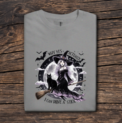 Gray t-shirt with witch graphic and text on a wooden surface