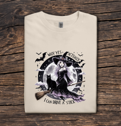 Beige t-shirt with witch graphic and text on a wooden surface