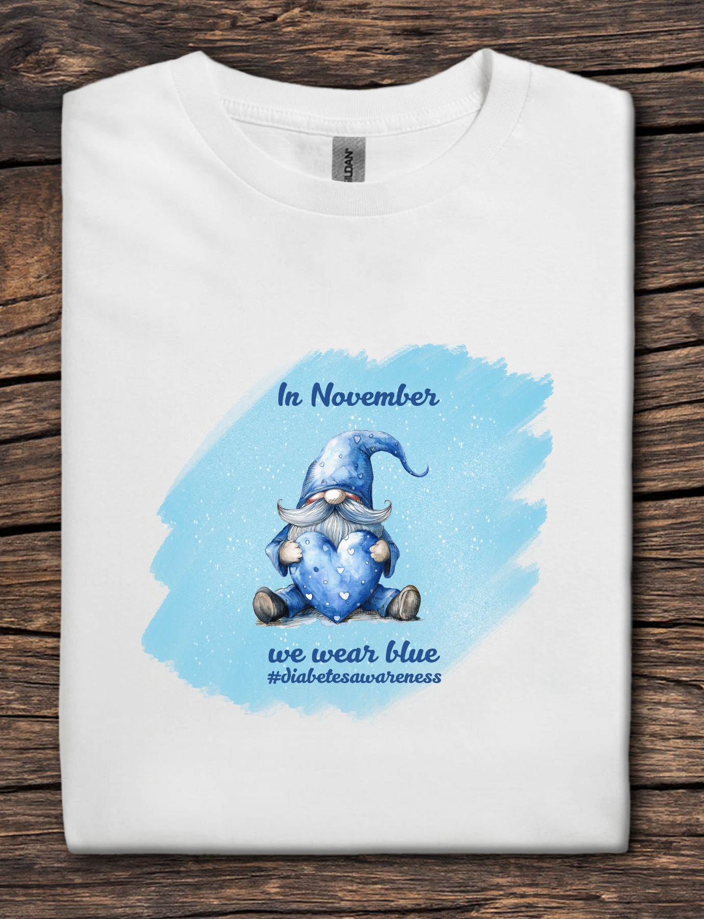 White t-shirt with a blue gnome graphic and text on a wooden surface