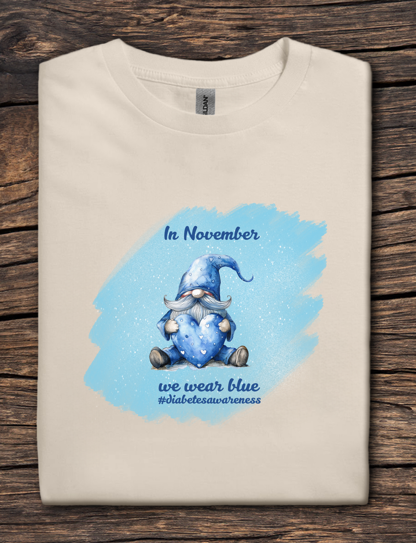 Beige t-shirt with a blue gnome graphic and text on a wooden surface