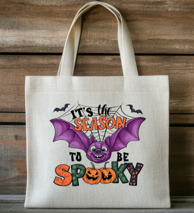 Tote bag with Halloween design featuring a bat and text on a wooden background
