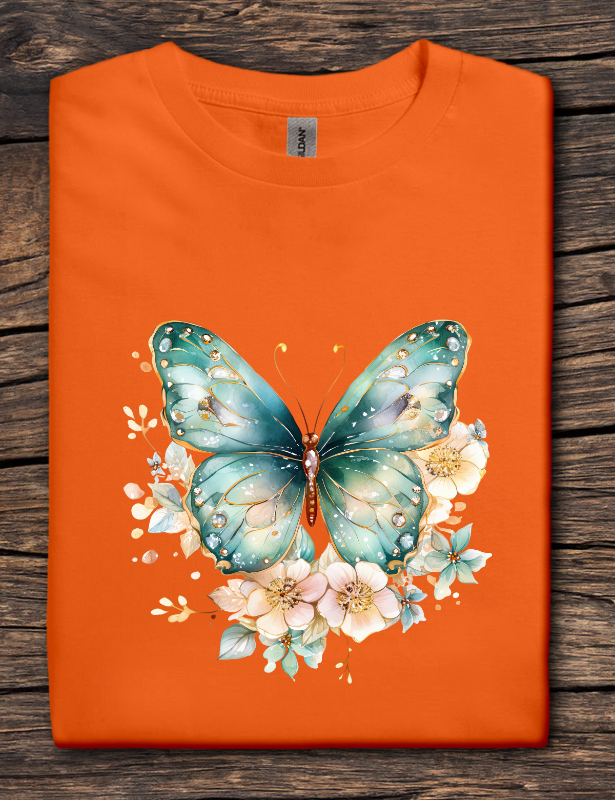 Orange t-shirt with a teal butterfly and floral design on a wooden surface