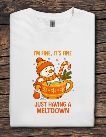 White t-shirt with a snowman in a mug graphic and text on a wooden surface