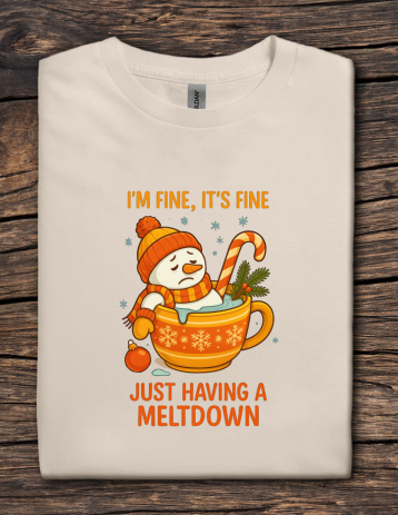 Folded t-shirt with a snowman in a mug graphic and text on a wooden surface