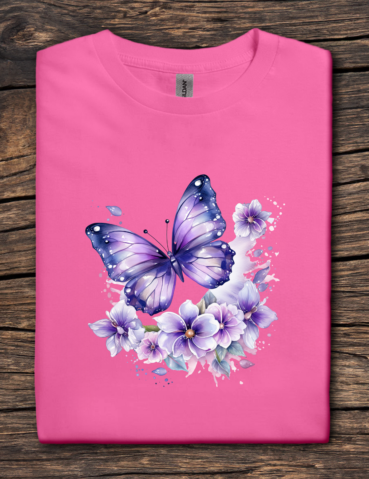 Pink t-shirt with a purple butterfly and flowers design on a wooden surface