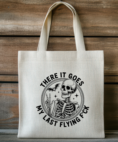 Beige tote bag with a graphic design featuring a skeleton and text on a wooden background