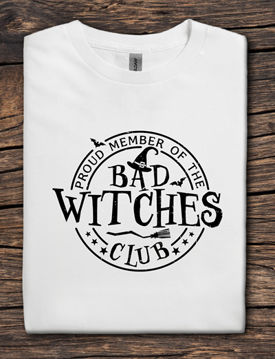 White t-shirt with 'Proud Member of the Bad Witches Club' text on a wooden surface