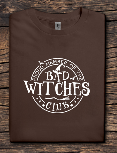 Brown t-shirt with 'Proud Member of the Bad Witches Club' text on a wooden surface
