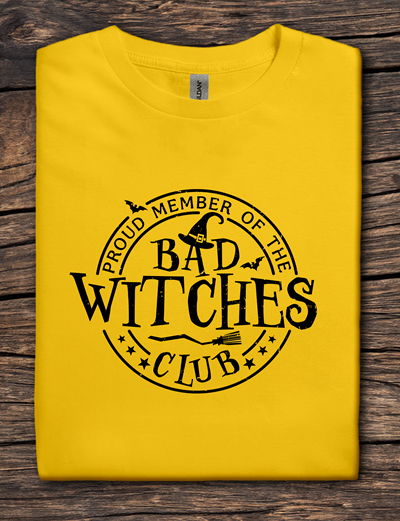 Yellow t-shirt with 'Proud Member of the Bad Witches Club' text on a wooden surface