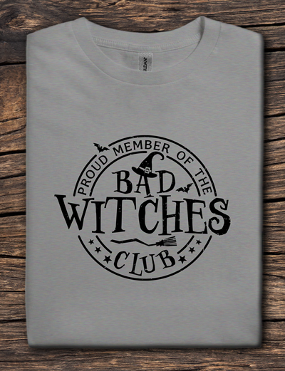 Gray t-shirt with 'Proud Member of the Bad Witches Club' text on a wooden surface
