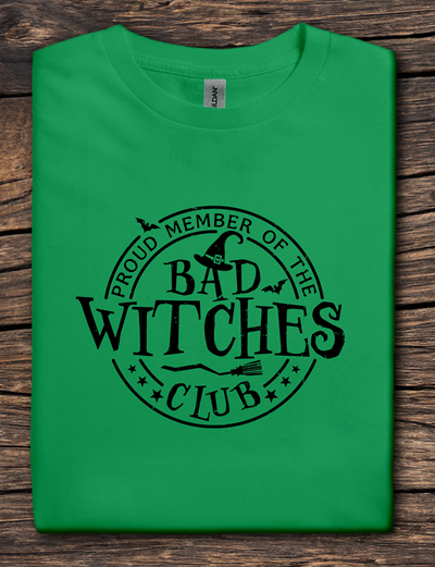 Green t-shirt with 'Proud Member of the Bad Witches Club' text on a wooden surface