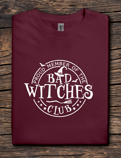 Maroon t-shirt with 'Proud Member of the Bad Witches Club' text on a wooden surface