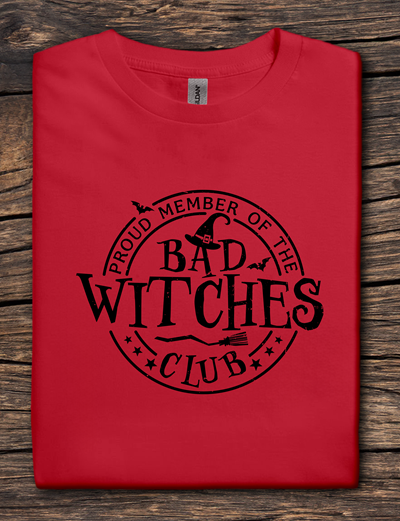 Red t-shirt with 'Proud Member of the Bad Witches Club' text on a wooden surface