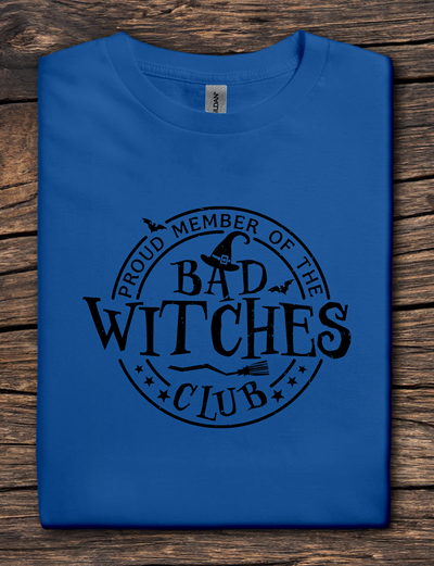 Blue t-shirt with 'Proud Member of the Bad Witches Club' text on a wooden surface