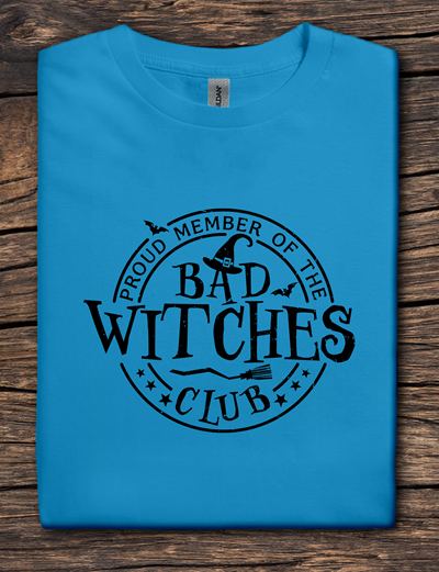 Blue t-shirt with 'Proud Member of the Bad Witches Club' text on a wooden surface
