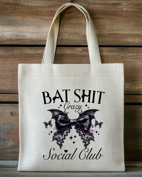 Natural canvas tote bag with gothic bat design and black bow reading “Bat Shit Crazy Social Club.”